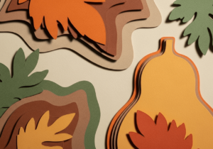 A closeup of paper cutouts of leafs of leaves, squash, and abstract shapes stacked on one another against a cream background
